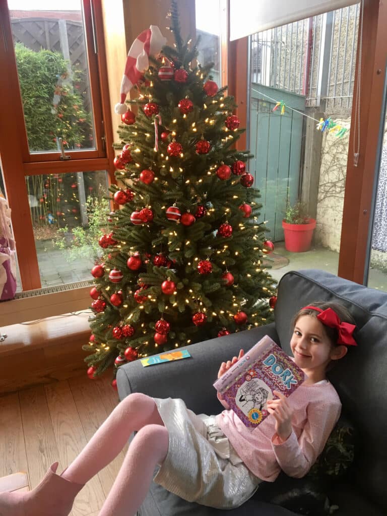 Little girl reading book beside Christmas tree